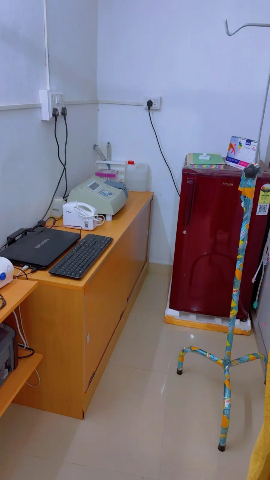 A corner with medical machines on a cabinet, a fridge and a drip stand
